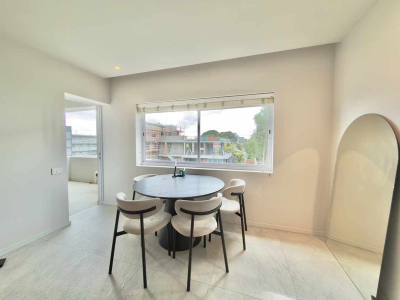 A bright and modern dining area featuring large windows, neutral tiled flooring, and recessed lighting, offering a clean and contemporary living space.