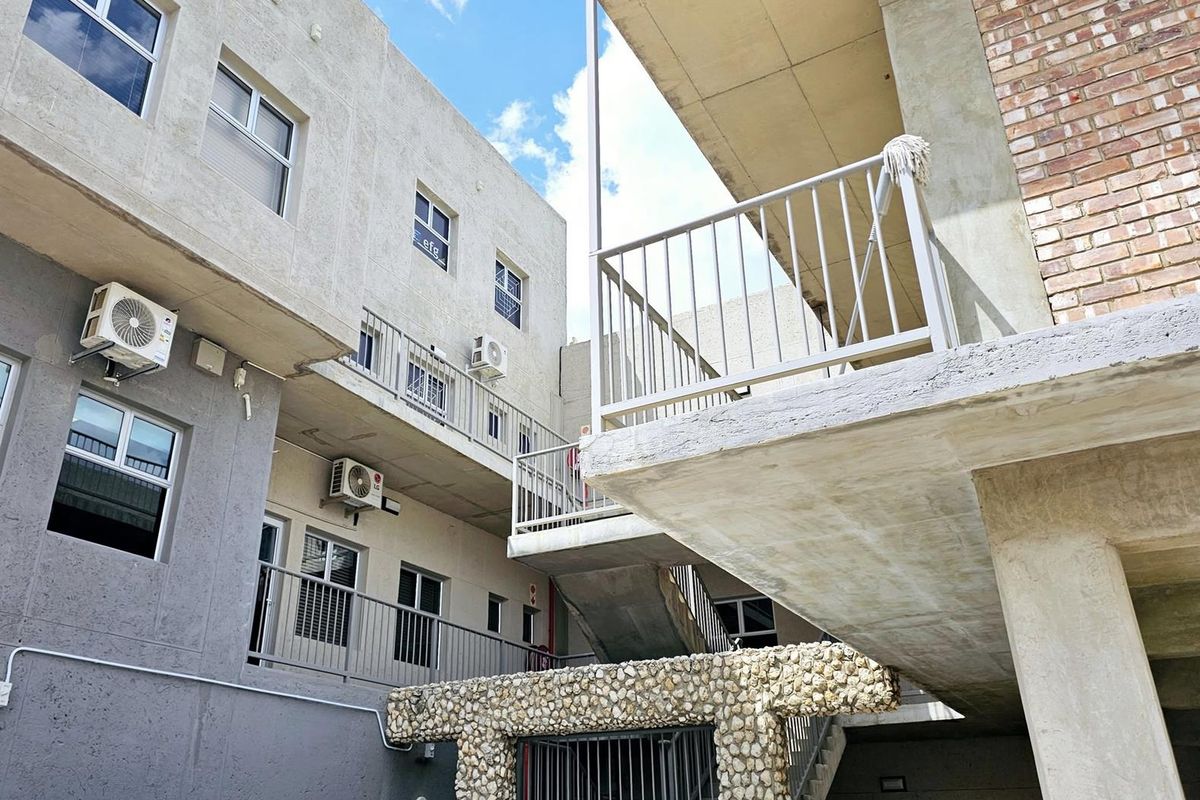 Exterior view of a multi-story office building featuring concrete walkways, metal railings, and external air conditioning units.