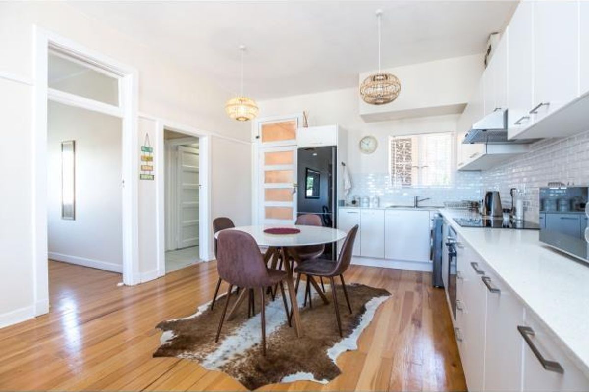 A bright, modern kitchen featuring white cabinetry, stone countertops, subway tile backsplash, and polished hardwood flooring, seamlessly integrated with a dining area.