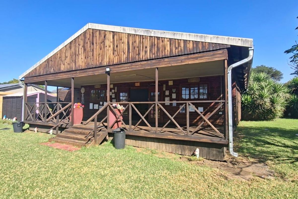 A rustic timber-clad farm building featuring a covered wrap-around veranda and wooden deck, set within a spacious garden area.