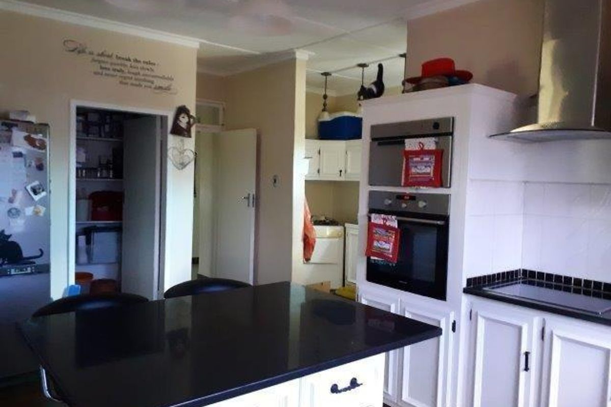 A functional kitchen featuring a central island, built-in oven and microwave, extractor fan, and a separate pantry area with white cabinetry.