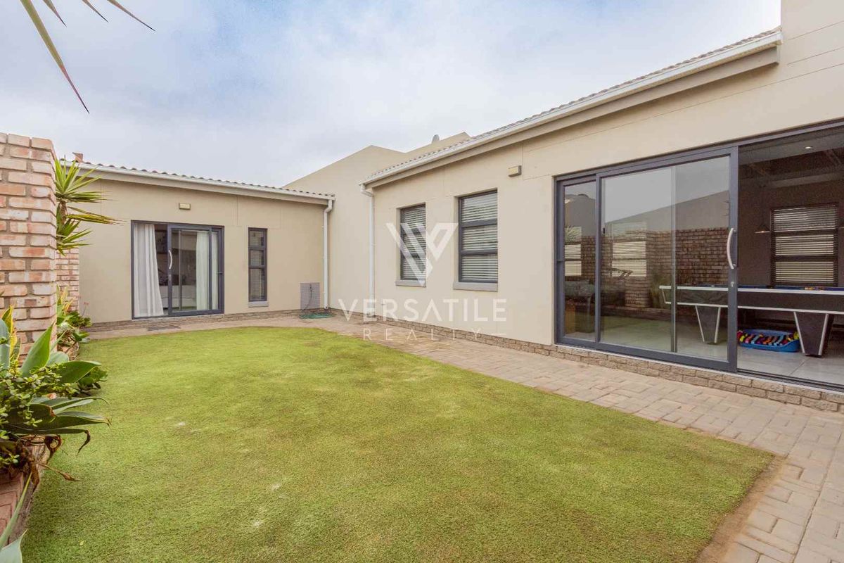 A well-maintained rear garden featuring a paved patio area and direct access to the home through large sliding glass doors.