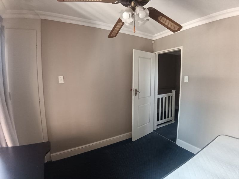 A vacant bedroom featuring neutral wall tones, carpeted flooring, a ceiling fan, and a built-in cupboard, with access to an adjacent hallway.
