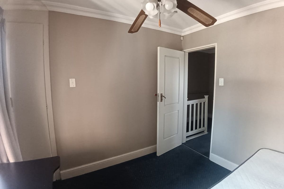 A vacant bedroom featuring neutral wall tones, carpeted flooring, a ceiling fan, and a built-in cupboard, with access to an adjacent hallway.