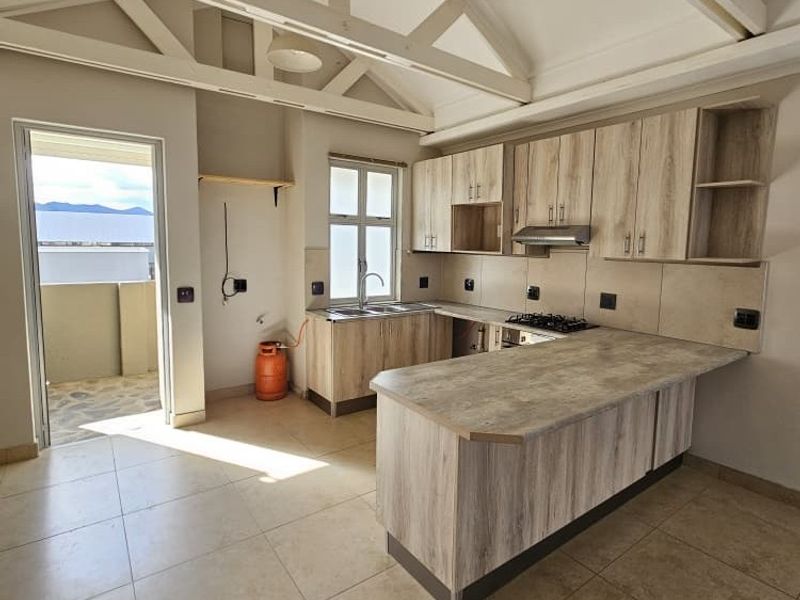Spacious kitchen featuring light wood-look cabinetry, laminate countertops, gas hob, and exposed roof trusses, leading out to a balcony.