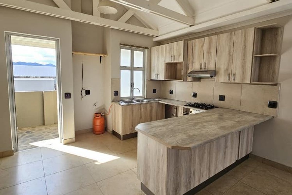 Spacious kitchen featuring light wood-look cabinetry, laminate countertops, gas hob, and exposed roof trusses, leading out to a balcony.