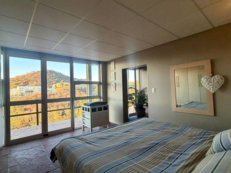 Spacious bedroom featuring large glass sliding doors that provide natural light and scenic hillside views, complemented by tiled flooring and built-in storage.