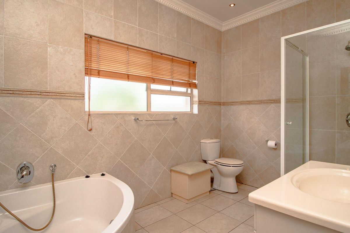 A well-maintained bathroom featuring a corner bathtub, separate shower enclosure, vanity basin, and neutral floor-to-ceiling wall tiling.