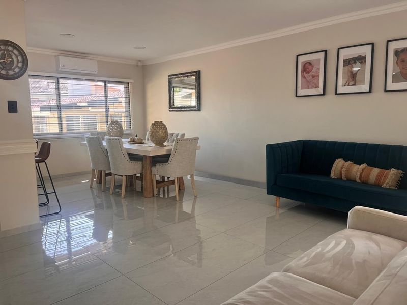 A bright open-plan living and dining area featuring polished porcelain floor tiles, recessed lighting, and a wall-mounted split-system air conditioner.