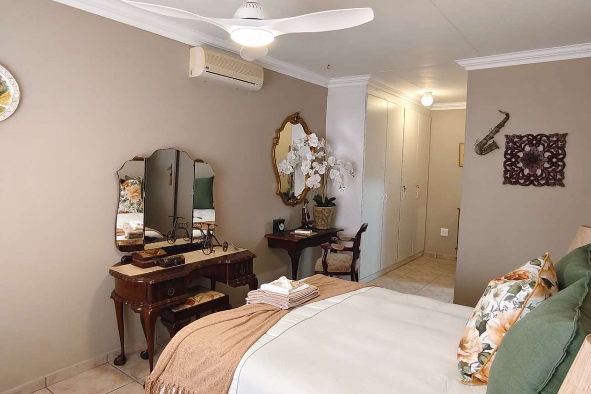 A well-maintained bedroom featuring tiled flooring, built-in cupboards, a ceiling fan, and a wall-mounted split-system air conditioner.