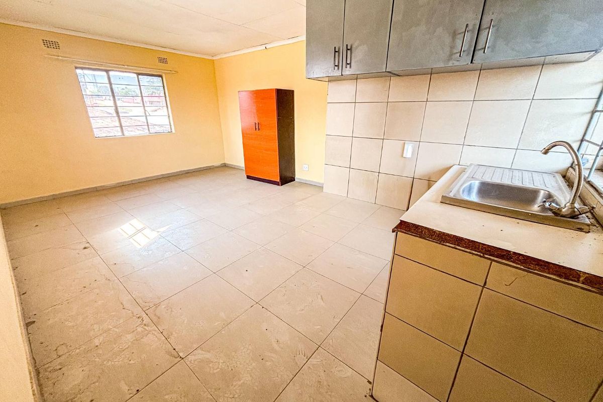 A functional kitchen space featuring tiled flooring, a stainless steel sink, and built-in upper cabinetry, offering a blank canvas for renovation.