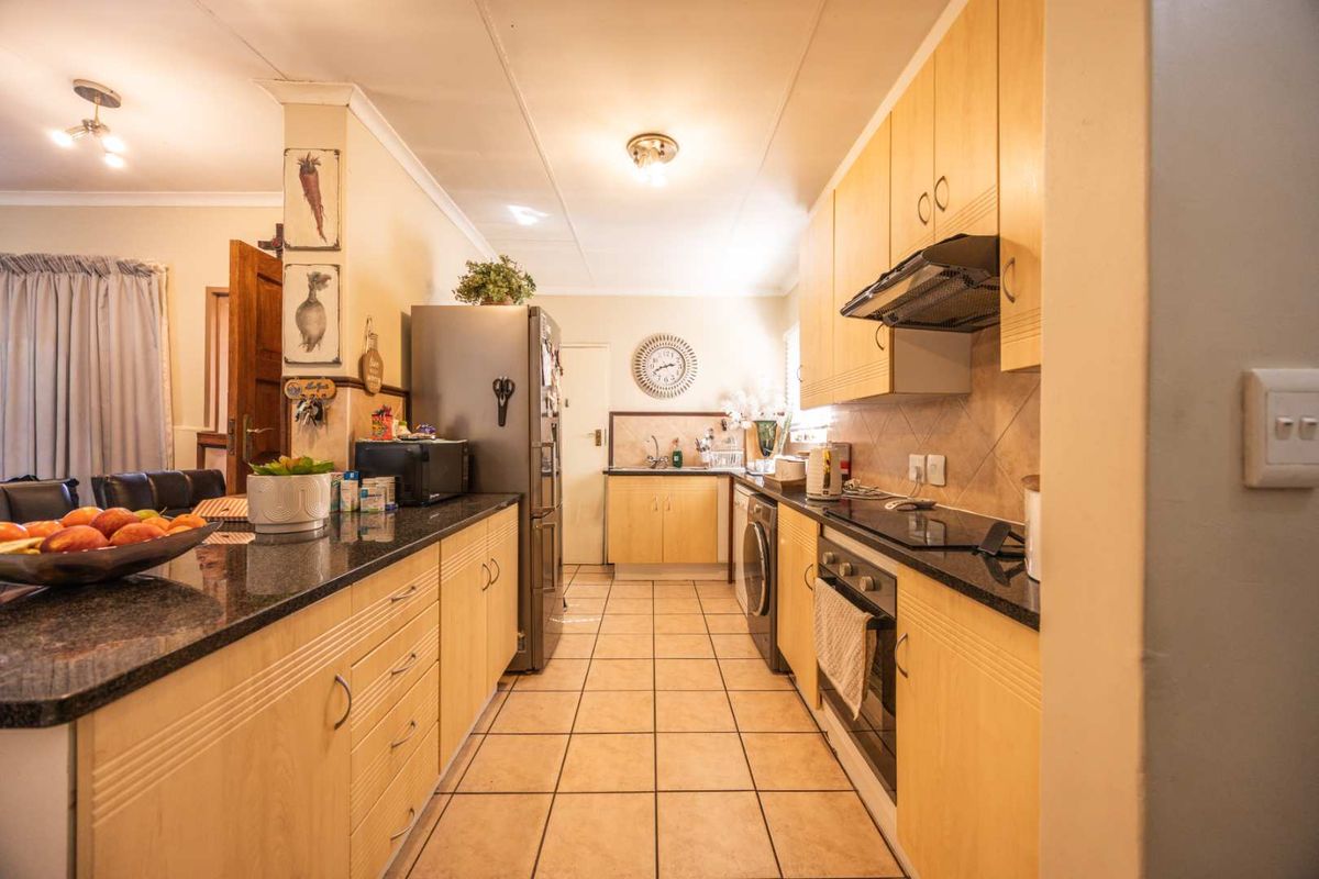 A functional galley-style kitchen featuring light wood cabinetry, granite countertops, integrated appliances, and tiled flooring, offering a practical layout for daily meal preparation.