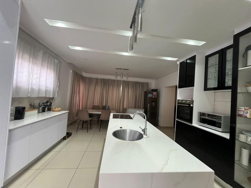 Modern open-plan kitchen featuring a large central island with stone countertop, integrated appliances, and sleek cabinetry, flowing into a dining area.