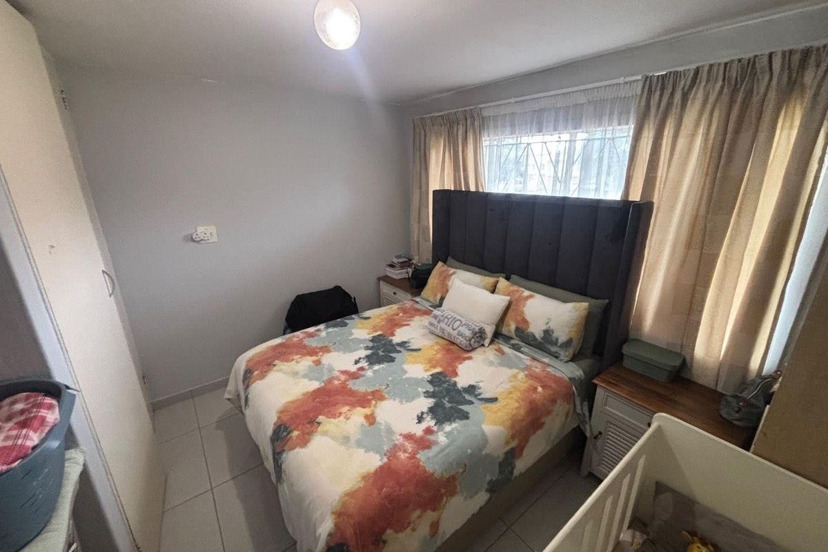 A functional bedroom featuring tiled flooring, built-in wardrobe, and a window with security bars.