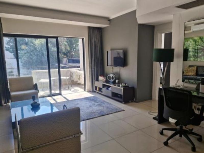 A bright, open-plan living area featuring large sliding glass doors that lead to a balcony, complemented by neutral tiled flooring and modern recessed lighting.