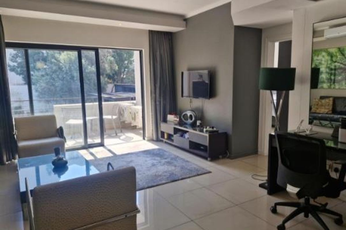 A bright, open-plan living area featuring large sliding glass doors that lead to a balcony, complemented by neutral tiled flooring and modern recessed lighting.