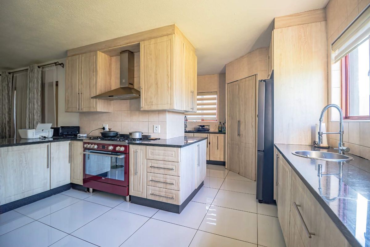 A well-maintained kitchen featuring light wood cabinetry, granite countertops, a gas stove with an extractor fan, and tiled flooring.