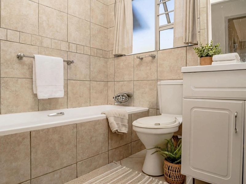 A functional bathroom featuring tiled walls, a built-in bathtub, a standard toilet, and a white vanity cabinet with a mirror.