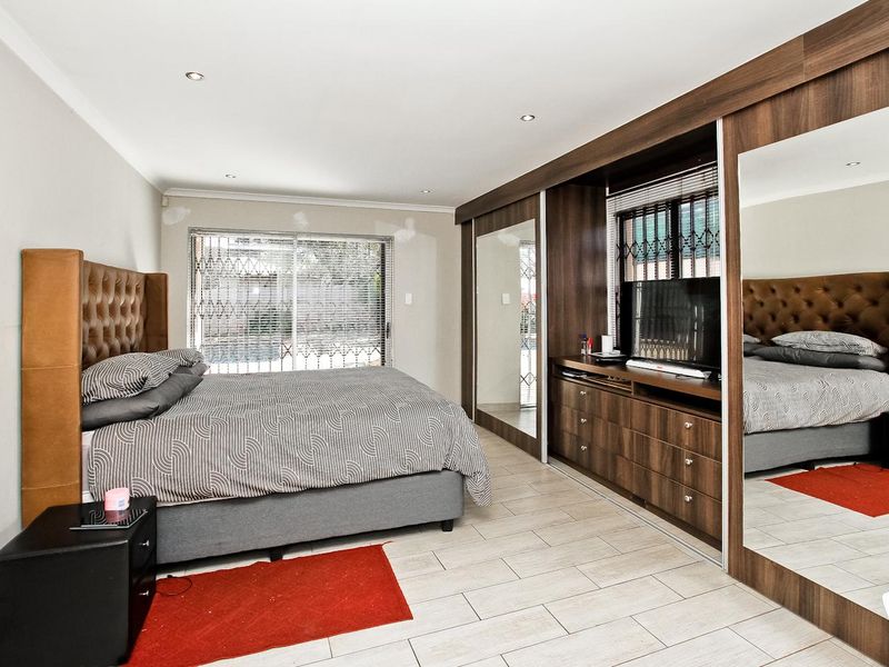 Spacious bedroom featuring extensive built-in cupboards with mirrored sliding doors, tiled flooring, and recessed lighting.
