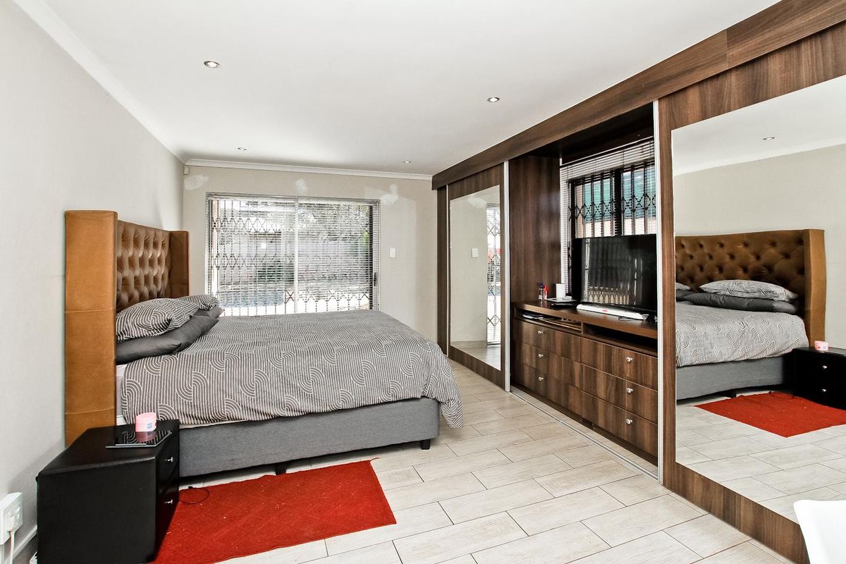 Spacious bedroom featuring extensive built-in cupboards with mirrored sliding doors, tiled flooring, and recessed lighting.