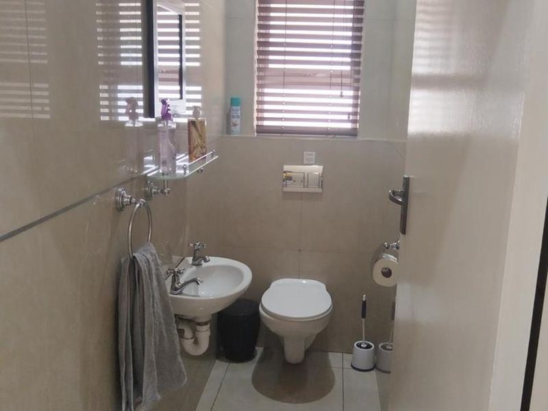 A compact, modern bathroom featuring a wall-mounted toilet, wall-mounted basin, and neutral floor-to-ceiling tiling.