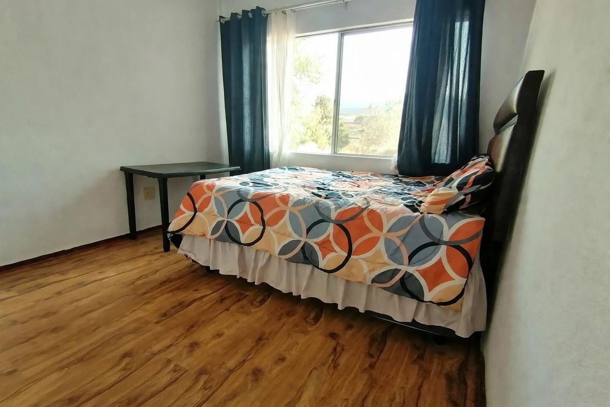 A functional bedroom featuring wood-look laminate flooring and a large sliding window providing natural light.
