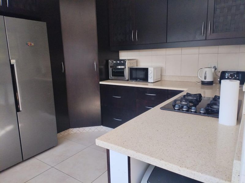 A functional kitchen featuring dark cabinetry, stone countertops, and a built-in gas hob with tiled flooring and backsplash.