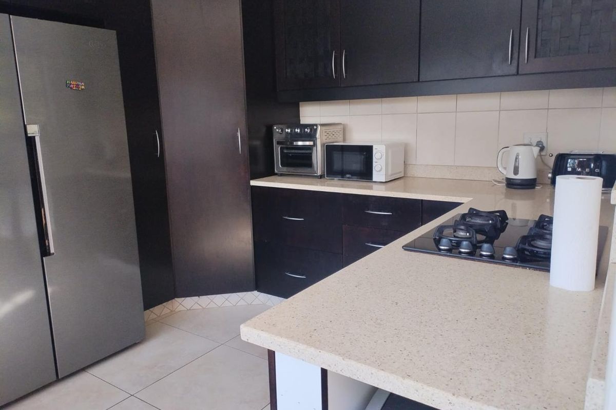 A functional kitchen featuring dark cabinetry, stone countertops, and a built-in gas hob with tiled flooring and backsplash.
