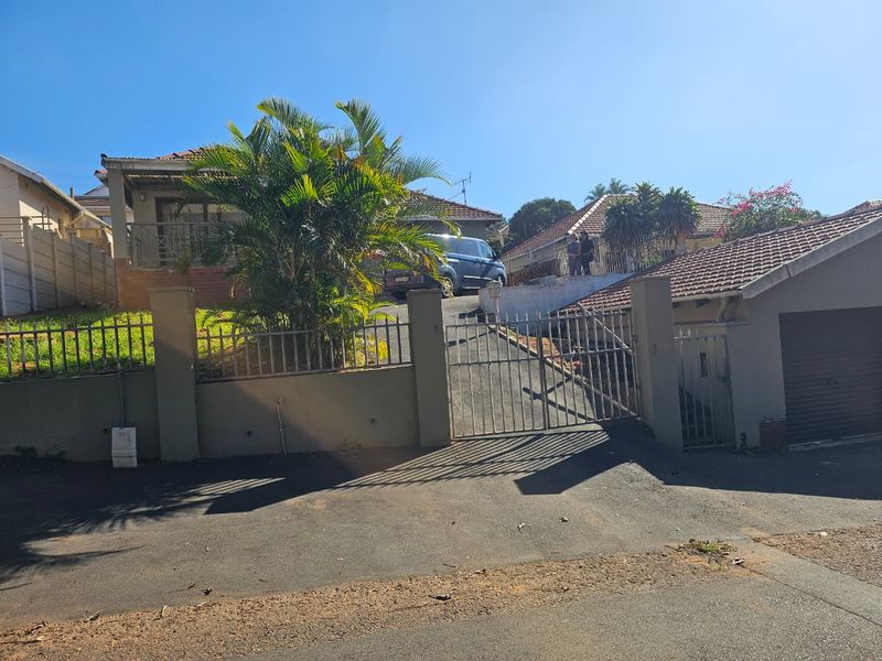 Front exterior view of the property featuring a gated driveway, concrete boundary wall, and tiled roof garage structure.