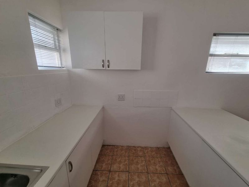 A functional laundry room featuring built-in cabinetry, laminate countertops, a stainless steel sink, and tiled flooring with dual windows.