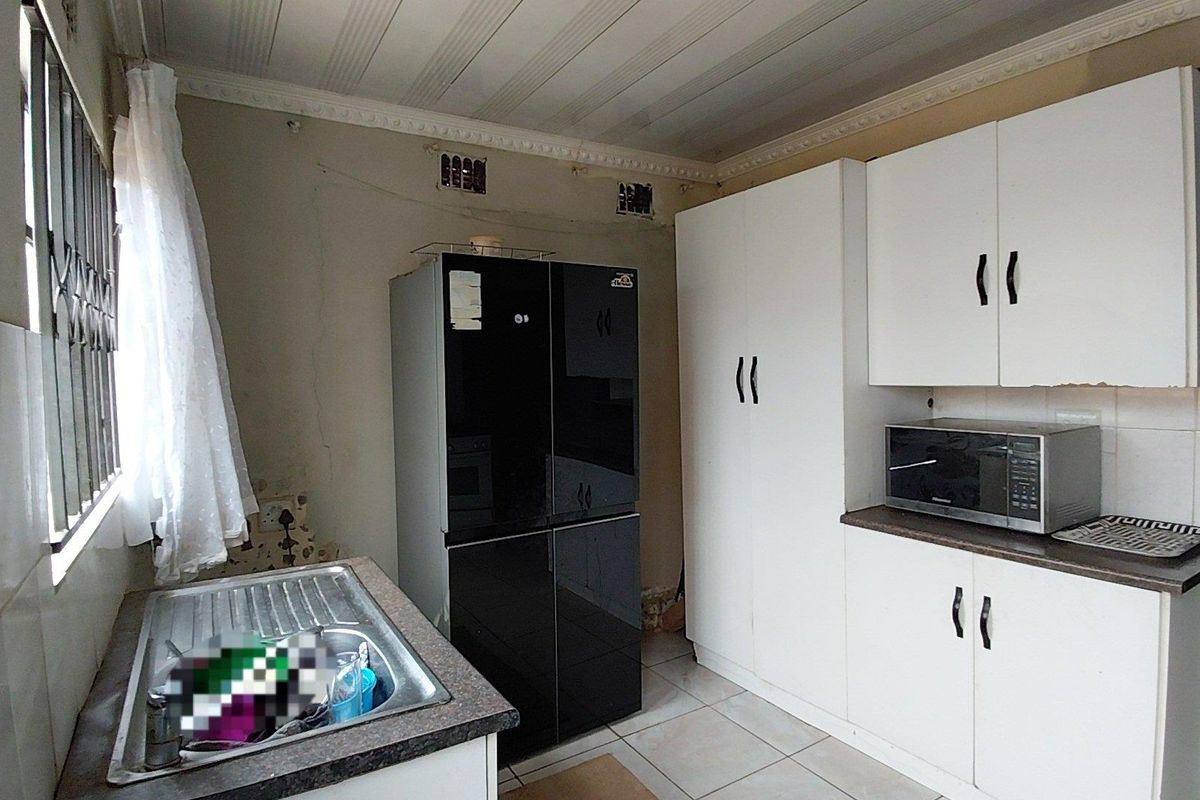 A functional kitchen featuring built-in cabinetry, a stainless steel sink, and tiled flooring, currently showing signs of wear and requiring cosmetic updates.