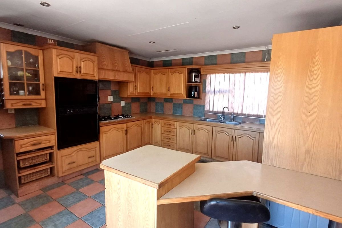 A spacious kitchen featuring extensive wooden cabinetry, built-in oven, gas hob, and a functional breakfast nook with tiled flooring and splashbacks.