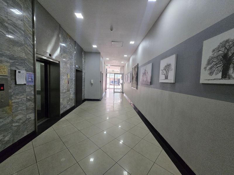 A well-maintained apartment building hallway featuring marble wall cladding, tiled flooring, and elevator access.