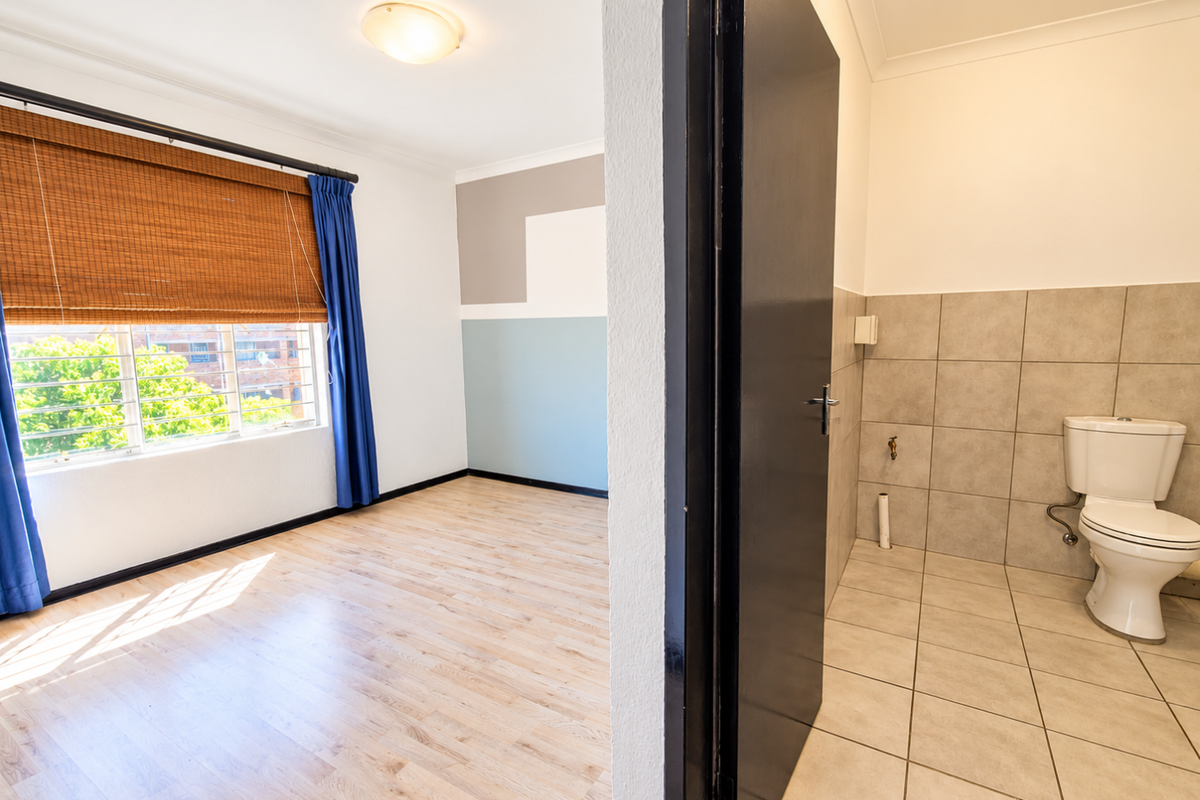 A bright, empty bedroom featuring laminate flooring and an adjacent tiled bathroom with a standard toilet fixture.
