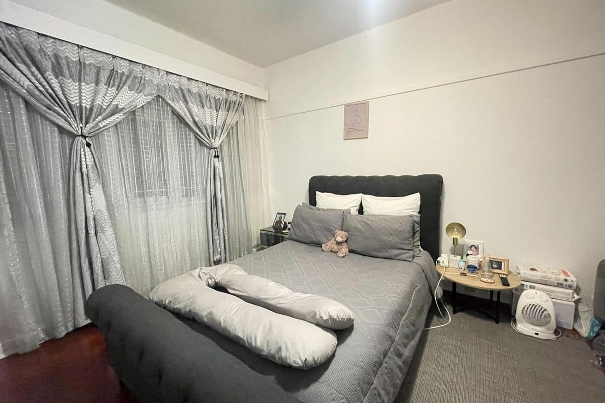 A cozy bedroom featuring hardwood flooring and a large window dressed with decorative curtains, providing a comfortable and functional sleeping space.