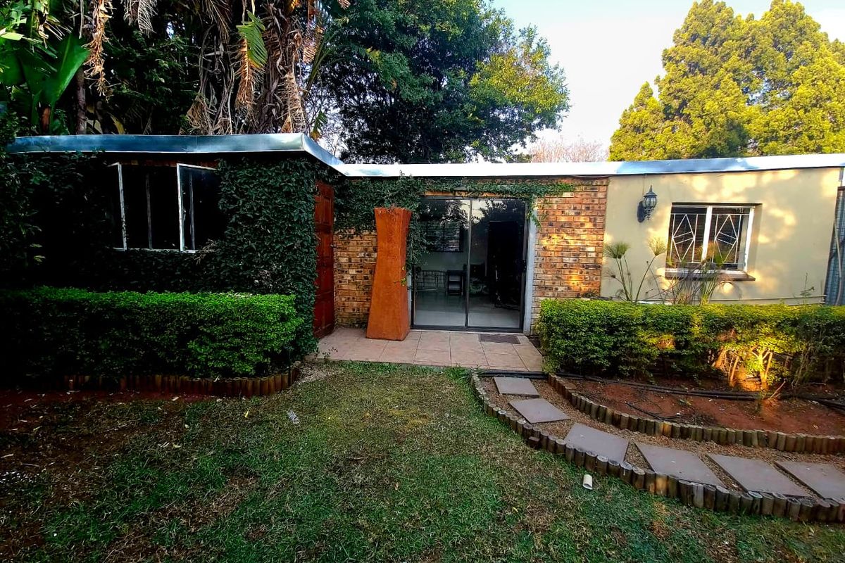 Rear exterior view of the property featuring a brick facade, sliding glass door access, and a landscaped garden with a stone pathway.