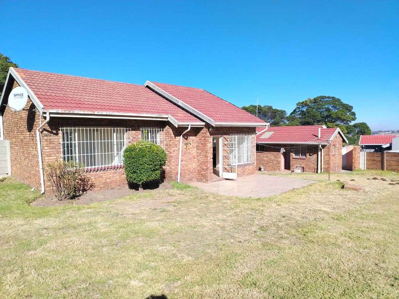 Rear view of a face brick house featuring a tiled roof, security bars on windows, and a paved patio area overlooking the garden.