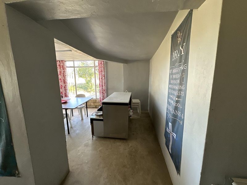 An open-plan living and dining area featuring a built-in counter, large windows, and neutral wall finishes, offering a blank canvas for renovation.