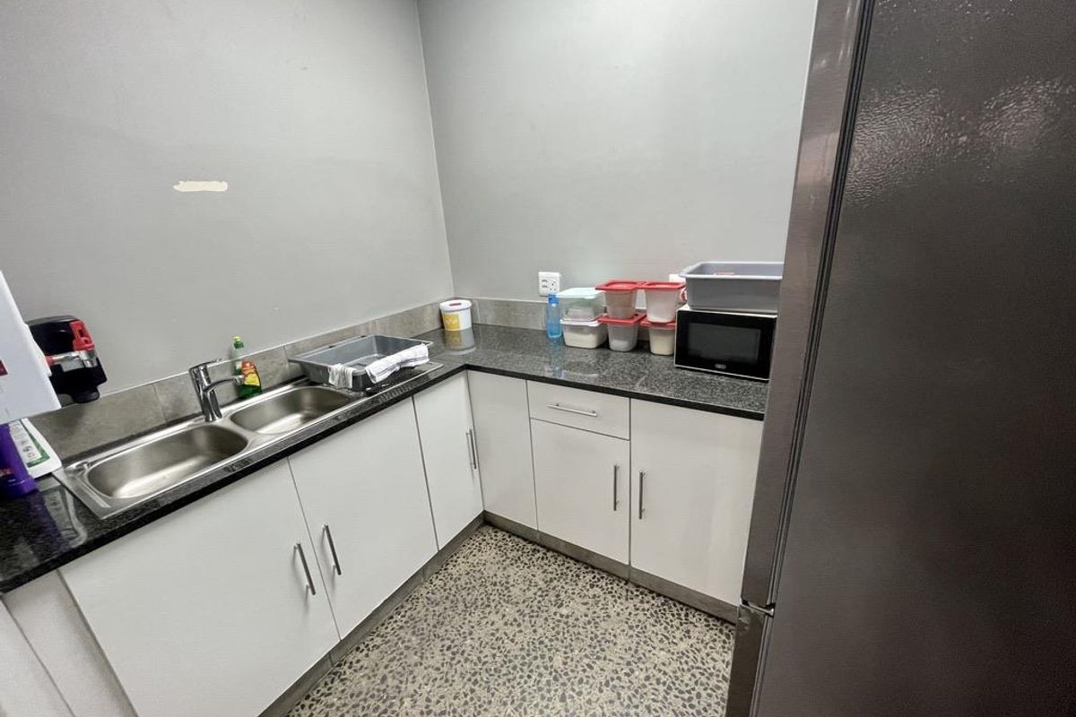 A functional kitchenette area featuring white cabinetry, dark granite countertops, a double stainless steel sink, and durable speckled flooring.