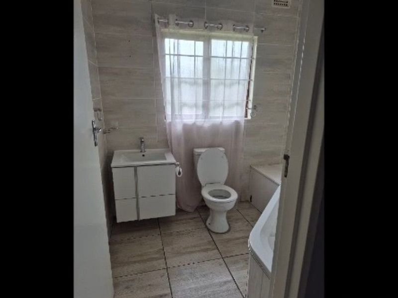 A functional bathroom featuring tiled walls and flooring, a vanity basin, a toilet, and a bathtub.