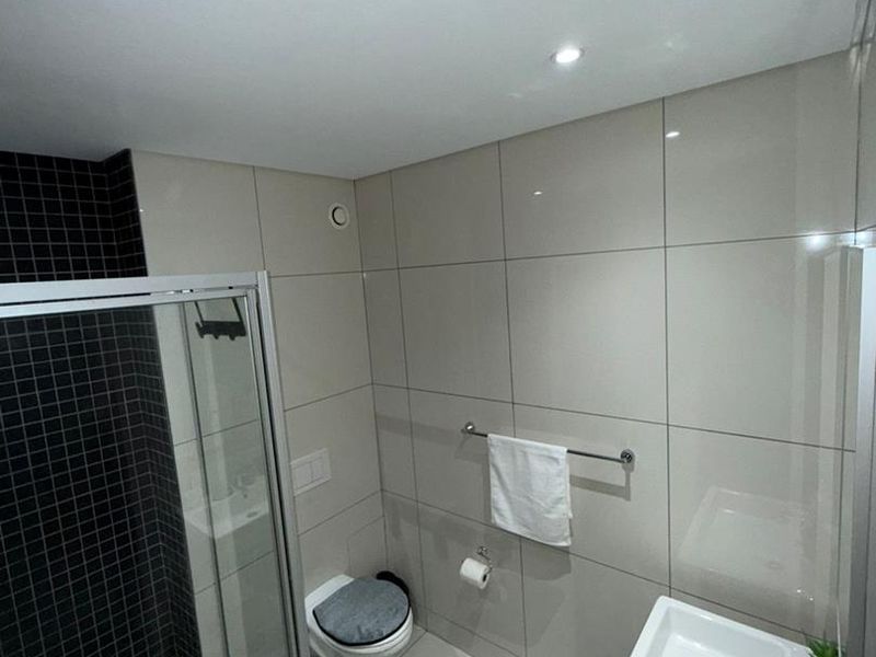 Modern bathroom featuring a glass-enclosed shower, wall-mounted toilet, and sleek basin with chrome fixtures, finished with contemporary neutral and black tiling.