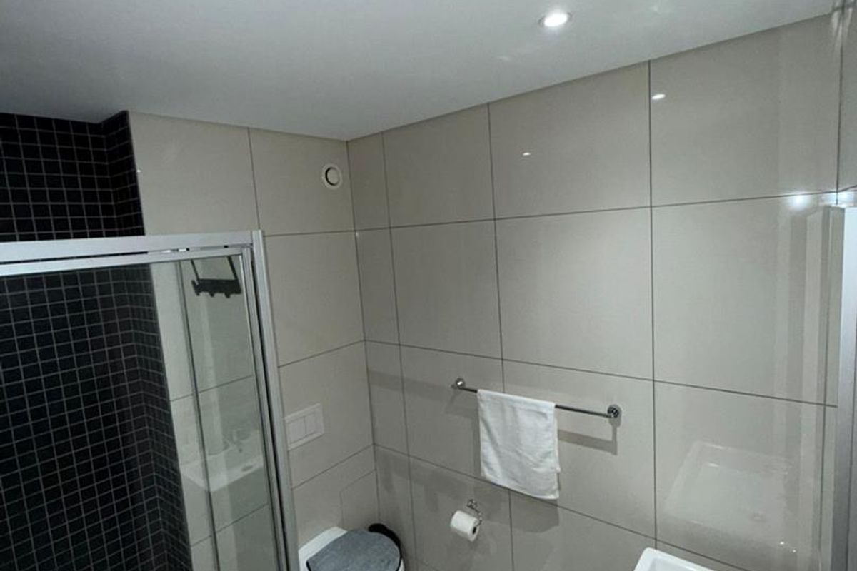 Modern bathroom featuring a glass-enclosed shower, wall-mounted toilet, and sleek basin with chrome fixtures, finished with contemporary neutral and black tiling.