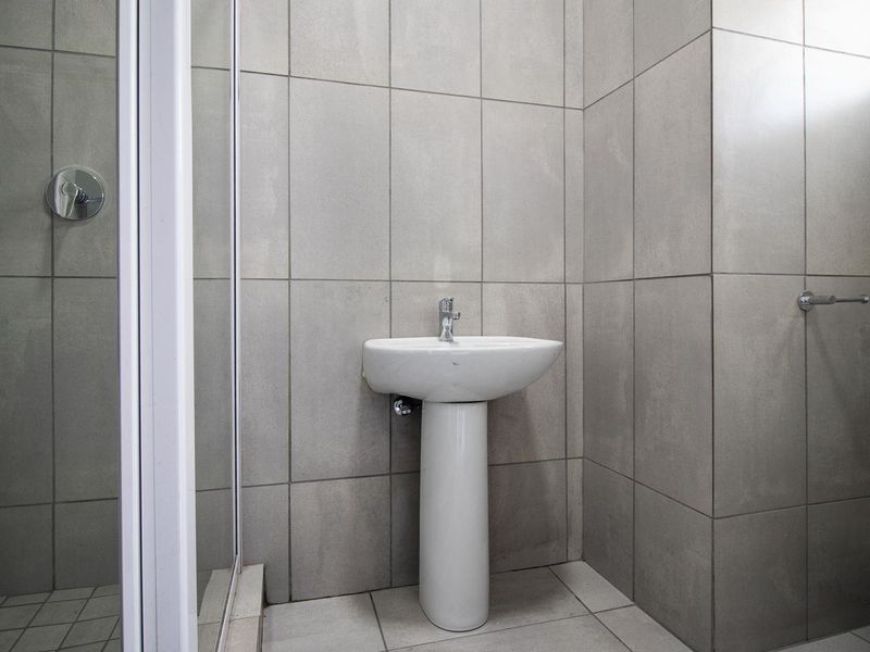 A clean, modern bathroom featuring grey ceramic wall tiles, a pedestal basin, a shower enclosure, and a standard toilet.
