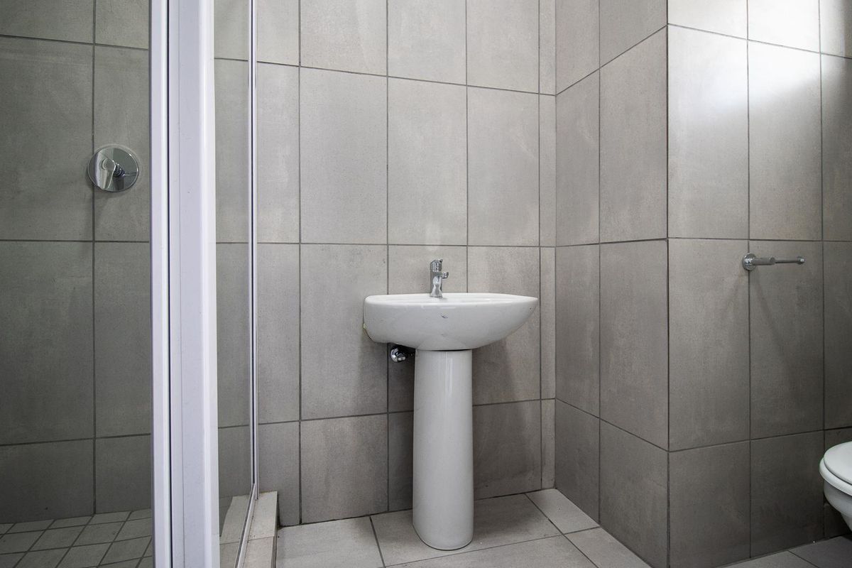 A clean, modern bathroom featuring grey ceramic wall tiles, a pedestal basin, a shower enclosure, and a standard toilet.