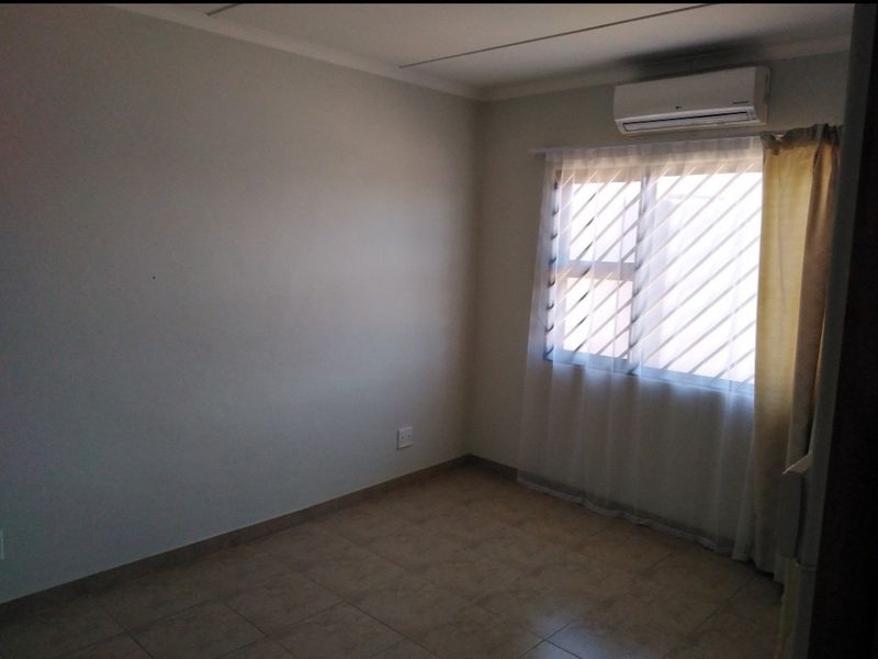A clean, empty bedroom featuring tiled flooring, neutral walls, and a wall-mounted air conditioning unit.
