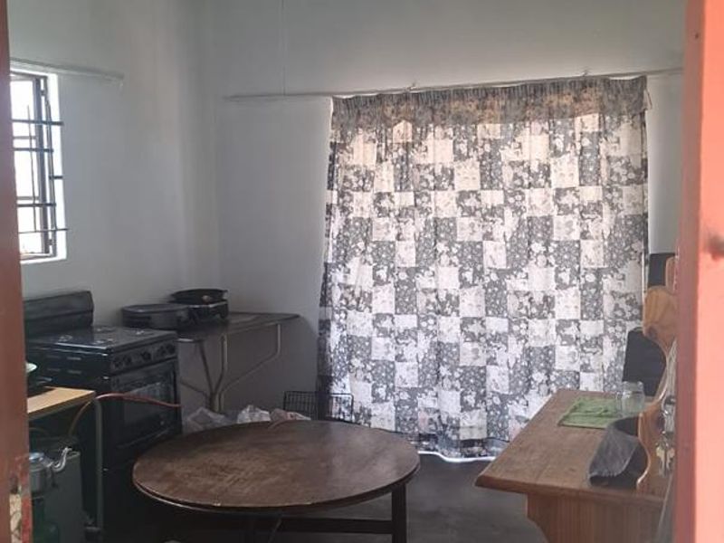 A rustic kitchen area featuring an exposed corrugated metal ceiling, a freestanding stove, and security bars on the window.