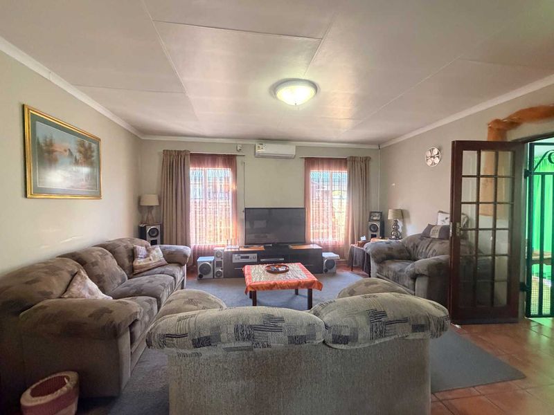 A comfortable living room featuring tiled flooring, a wall-mounted air conditioning unit, and a classic French door entrance.