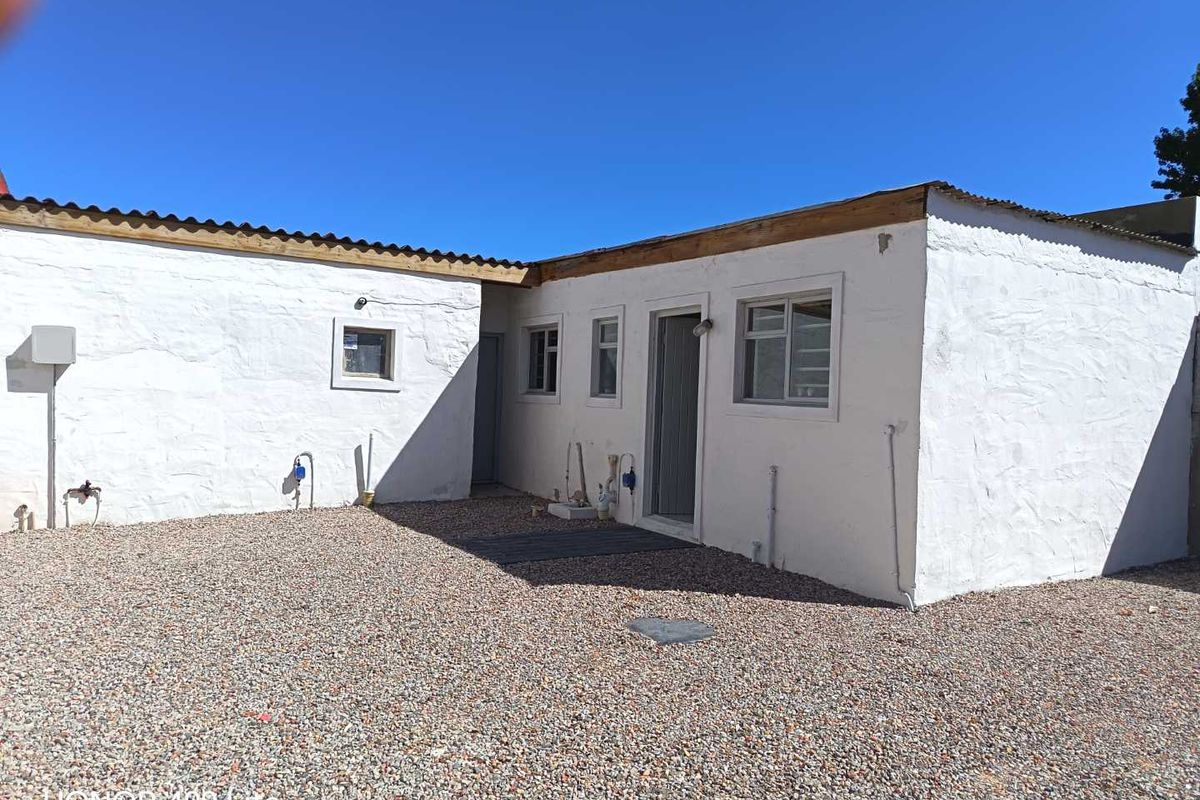 Rear exterior view of the cottage featuring plastered masonry walls, corrugated metal roofing, and a gravel courtyard area.