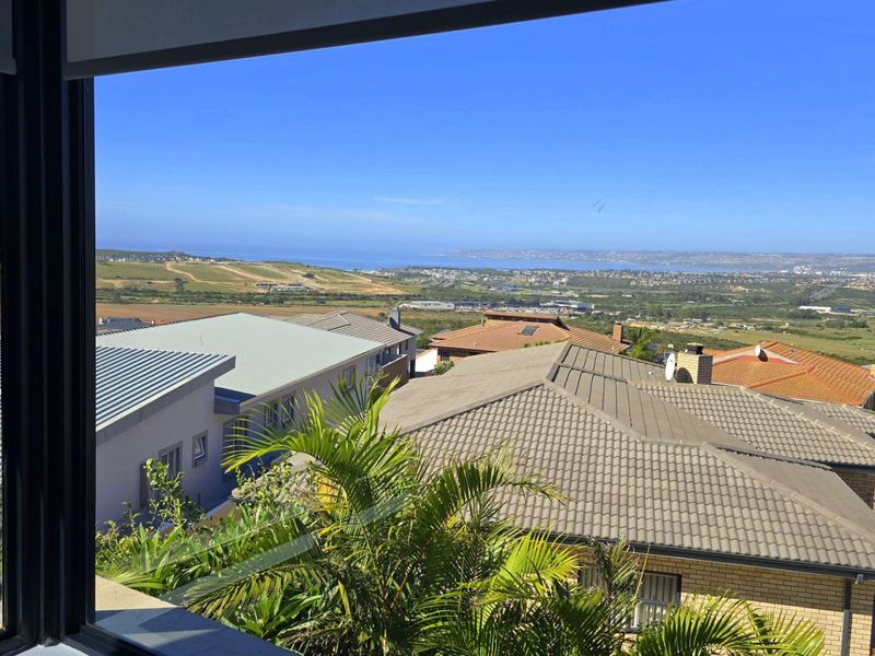 An elevated view overlooking the surrounding residential neighbourhood and distant coastal landscape, captured through a large window.