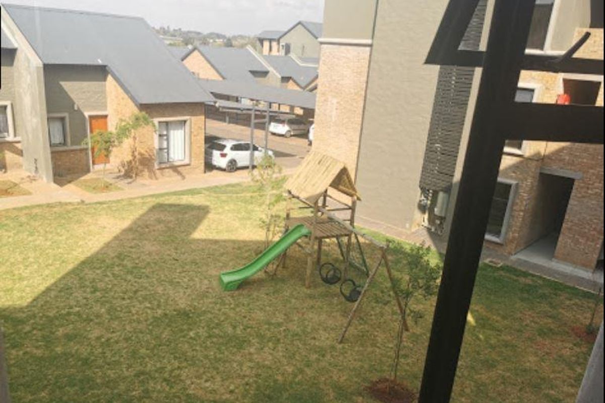 View of a communal garden area within the apartment complex, featuring a small playground and surrounding residential brick buildings.